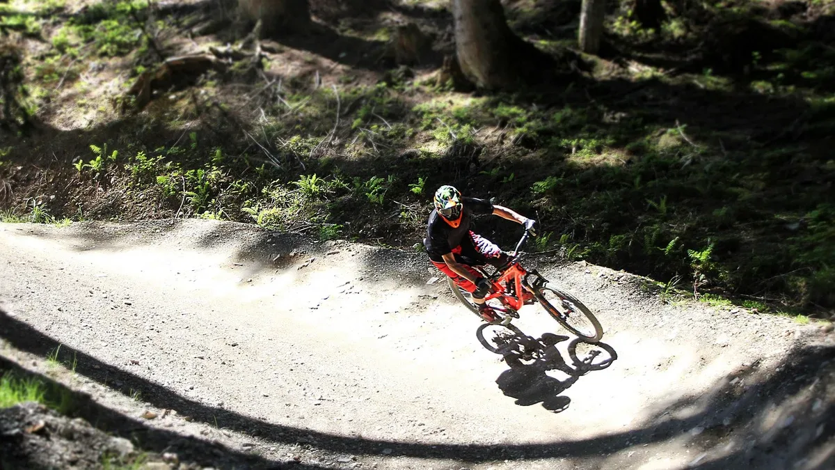 Bike park: rowerzysta w kasku full face przejeżdża bandę na leśnej trasie flow