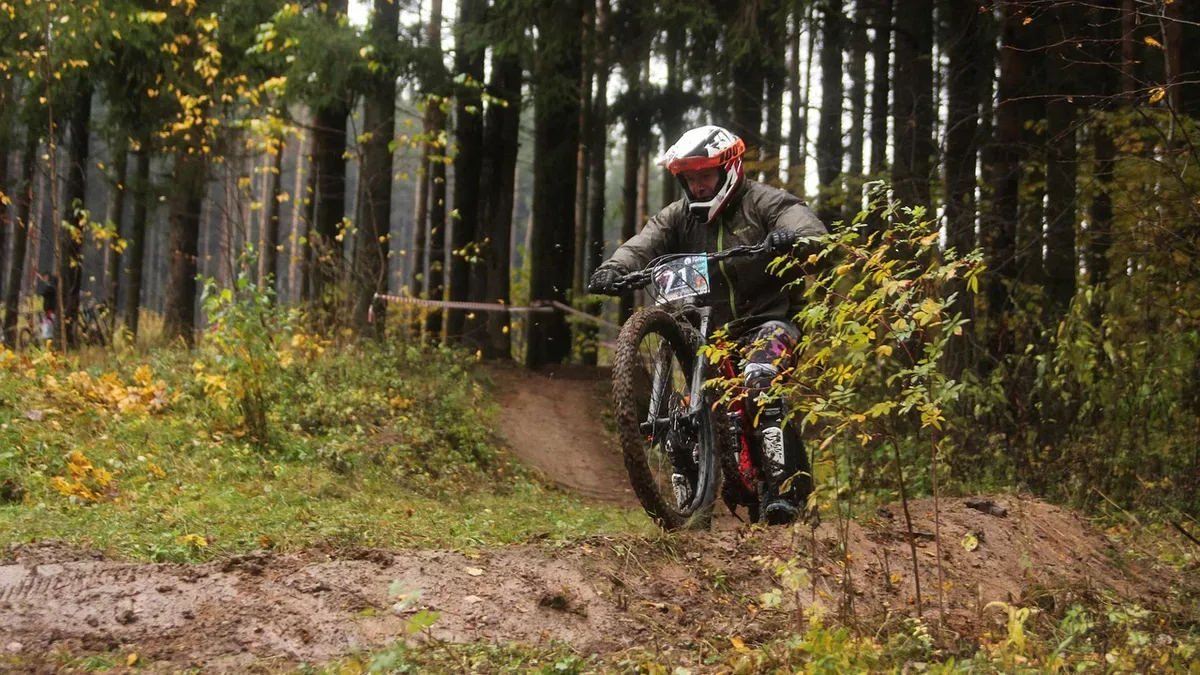 Pozycja na rowerze MTB na zjeździe: rowerzysta w kasku full face stoi na pedałach na leśnej trasie