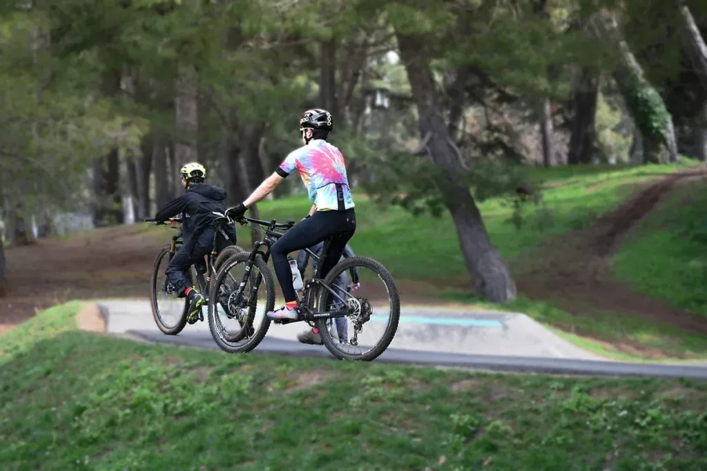 Rodzic z dzieckiem na rowerach przy pumptracku w leśnym parku