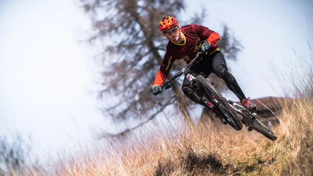 Rowerzysta w kasku, rękawiczkach i ochraniaczach kolan pochyla rower enduro w zakręcie