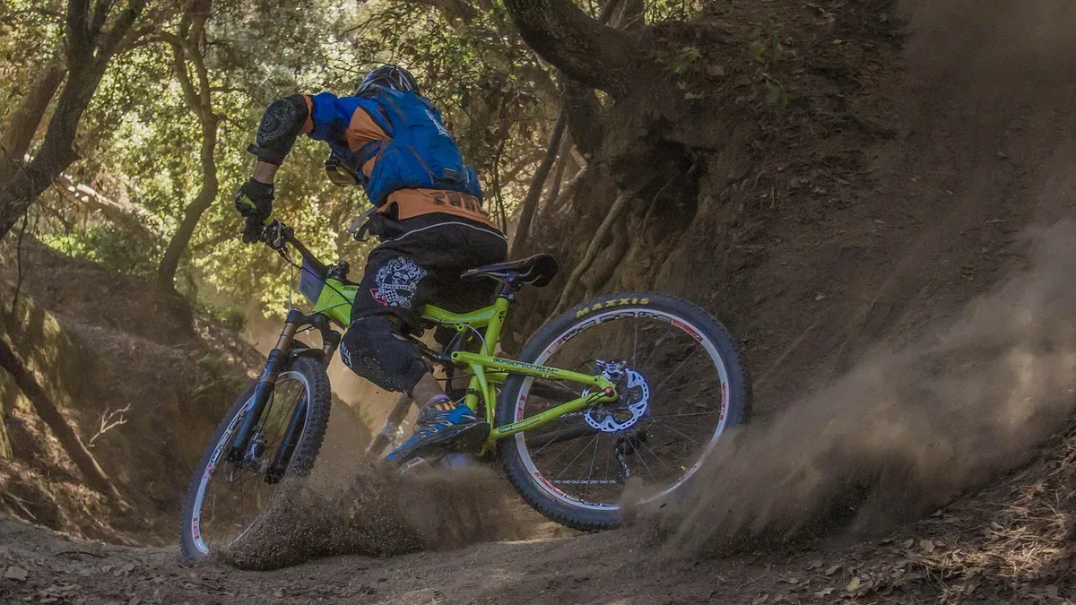 Rowerzysta enduro w kasku i ochraniaczach pokonuje bandę na zjeździe