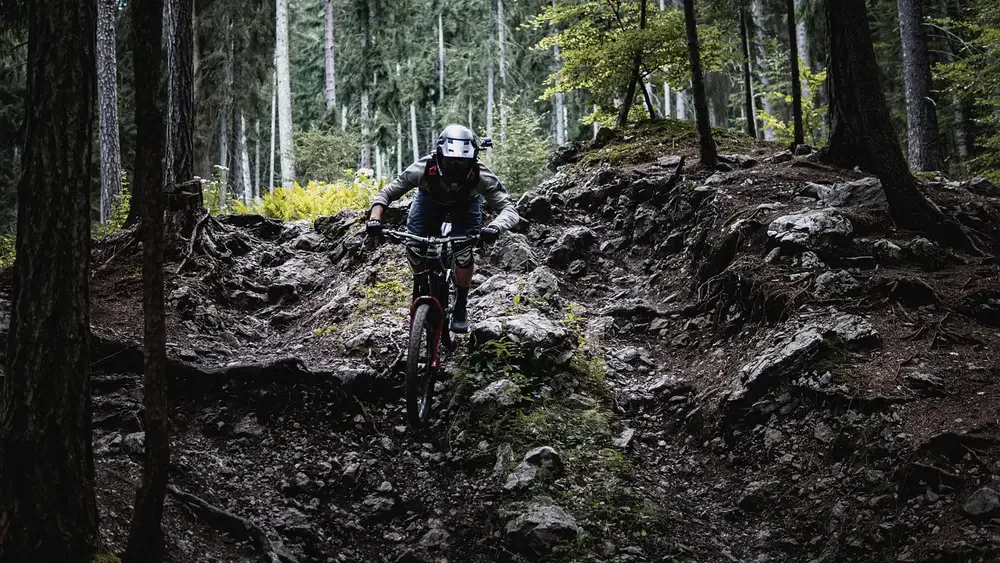 Zjazd enduro po skalistym leśnym odcinku, rowerzysta w pełnym kasku